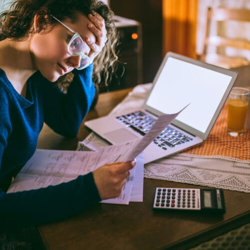 woman with calculator and laptop, worried about bills
